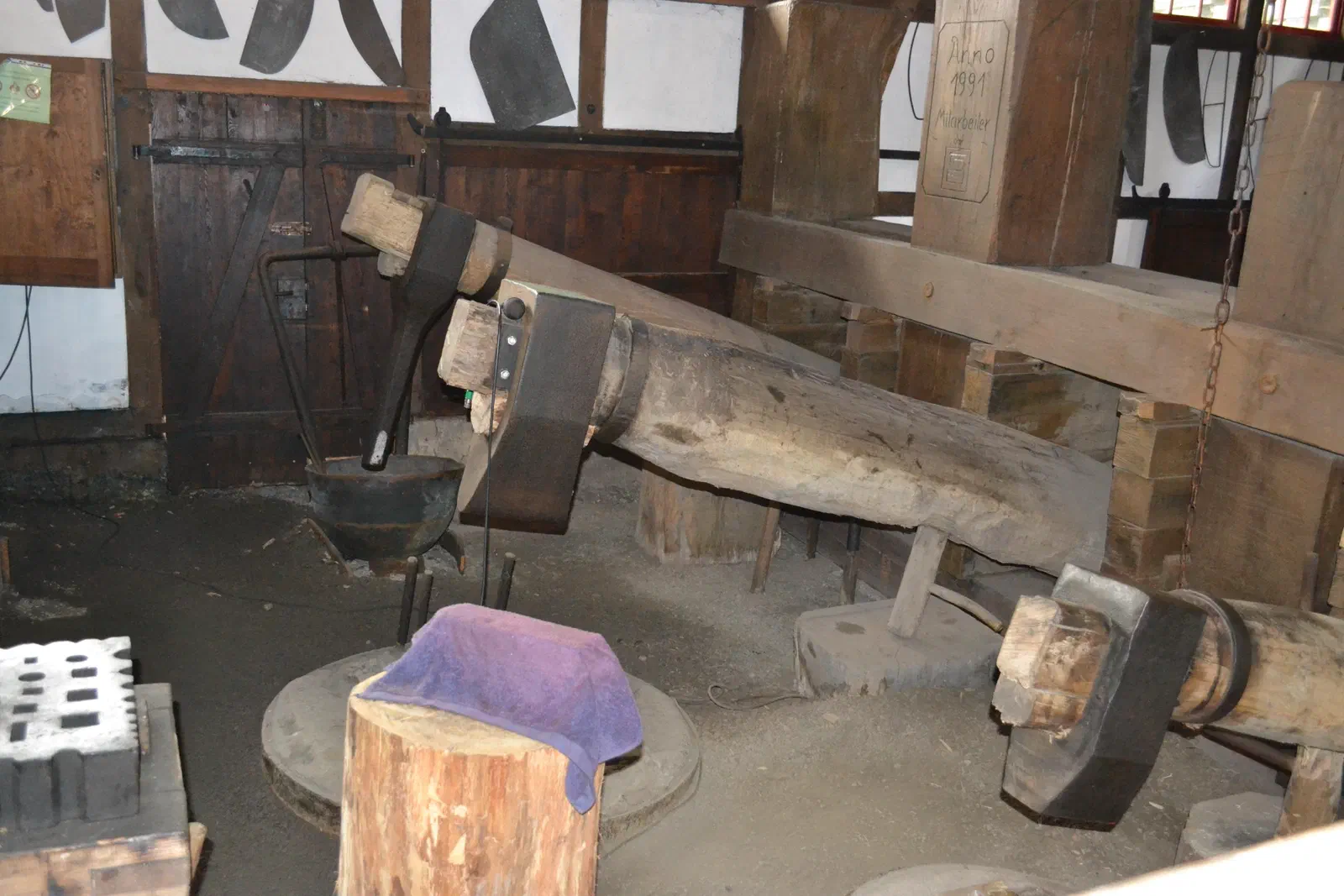 Historischer Fallhammer im Tobiashammer Ohrdruf: schwere Hämmer an langen Holzbalken über einem Amboss in der alten Schmiedehalle