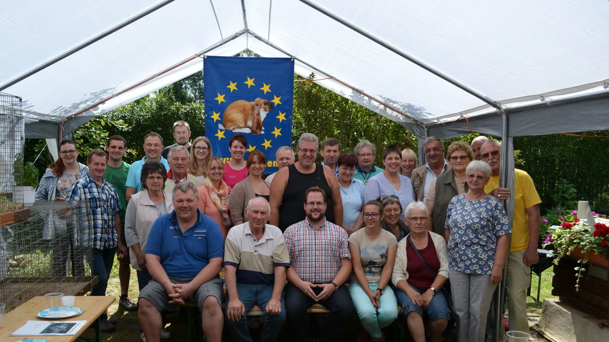 Gruppenfoto der Teilnehmer des IG-Treffens 2017 unter einem weißen Zelt, in der Mitte eine blaue Fahne mit Sternenkranz und Kaninchenbild