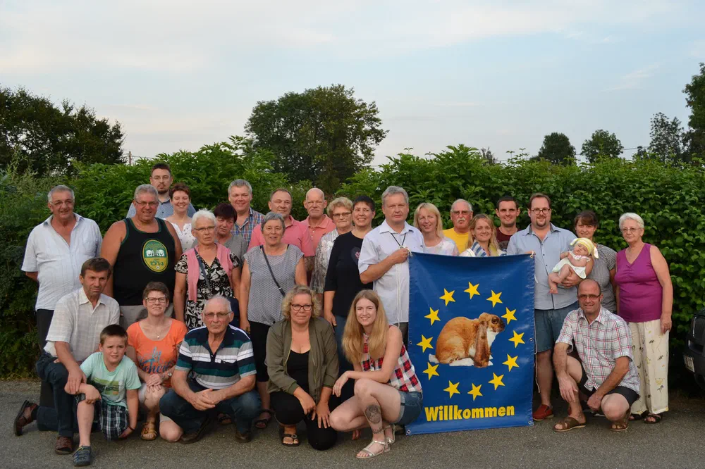 Gruppenfoto der Teilnehmer des IG-Treffens 2018 vor einer Hecke, vorne halten einige eine blaue Fahne mit Kaninchenbild und der Aufschrift „Willkommen“