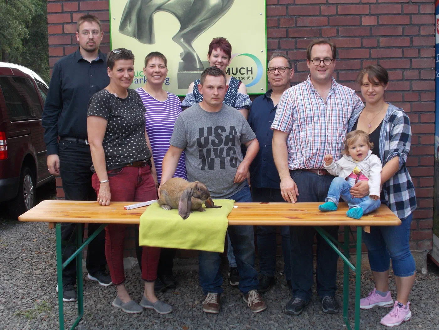 Gruppenfoto der Teilnehmer des IG-Treffens 2019 vor einer Backsteinwand, vorne auf einem Biertisch sitzt ein Englischer Widder auf einer grünen Decke