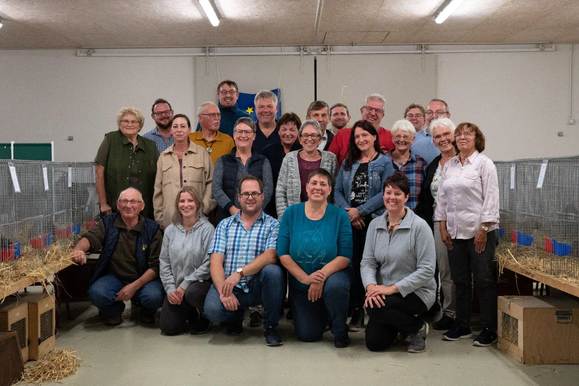 Photo de groupe des participants sur deux rangs dans une halle, à gauche et à droite des cages d'exposition avec de la paille