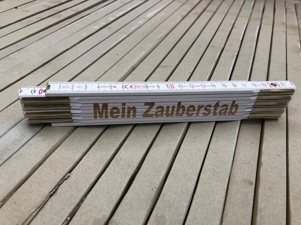 Zusammengeklappter weißer Holz-Zollstock mit Messingbeschlägen und der Aufschrift „Mein Zauberstab“